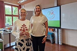 Die Schulleiterinnen Ursula Preininger und Simone Micheler stehen in einem Klassenzimmer vor einer digitalen Tafel. Auf der Tafel ist das Logo der Grundschule Krumbach zu sehen.